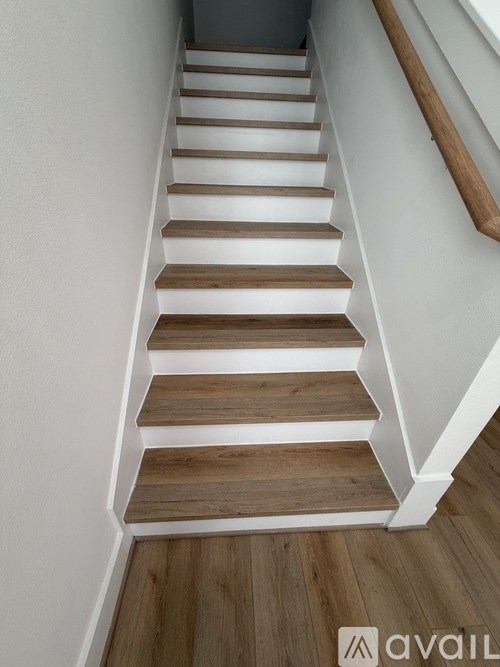 A set of wooden stairs with white risers and a wooden handrail.