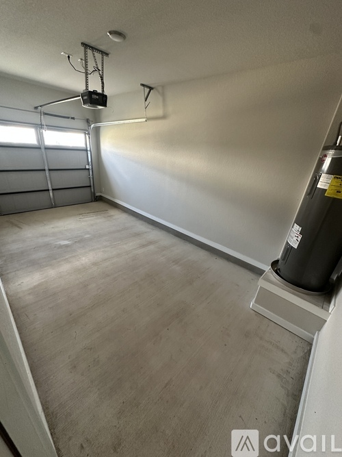 A room with a wooden floor and a white wall with a garage door opener on the wall.