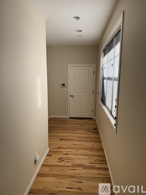 A long hallway with a white door and wooden floor.
