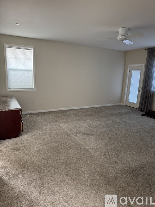 A room with a carpeted floor, a ceiling fan, and a window with blinds.