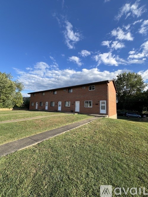 A red brick building with white doors and windows sits in a grassy field.