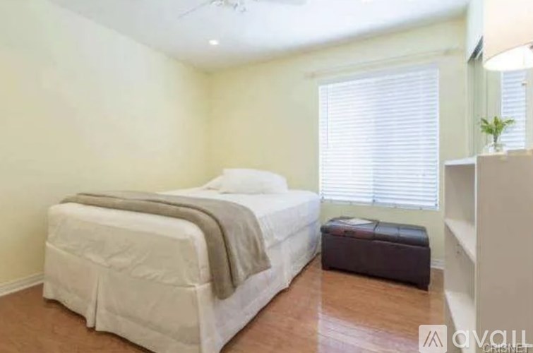 A bedroom with a bed, a bench, and a window with blinds.