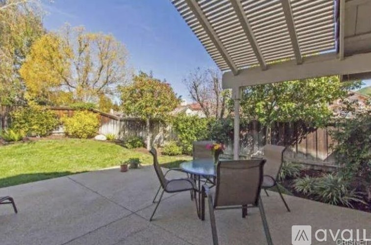 A patio with a table and chairs is surrounded by greenery.