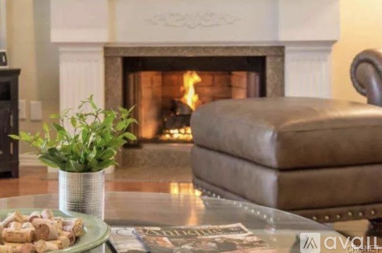 A living room with a fireplace and a brown leather ottoman.