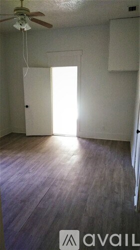 A room with a ceiling fan and a door leading to bright sunlight.