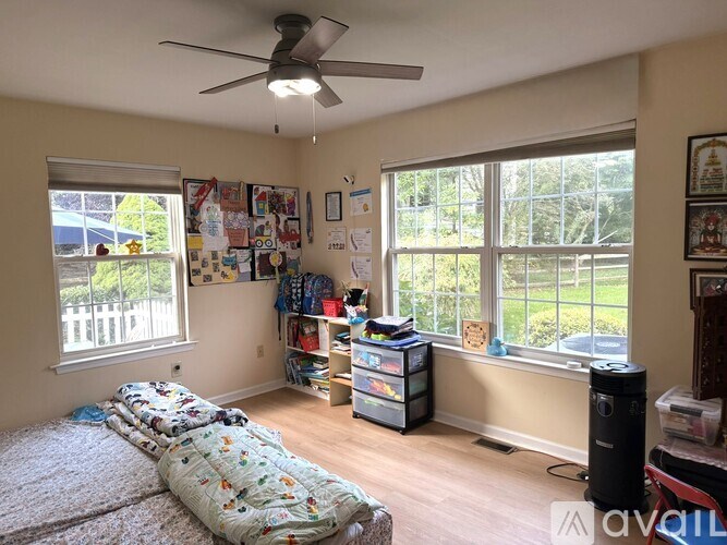 A room with a bed, a window, a fan, and a bookshelf.