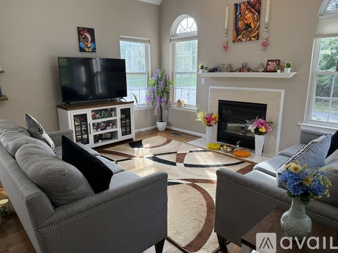 A living room with a grey couch, a television, a fireplace, and a vase of flowers.