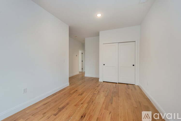 A room with wooden floors and white walls, with a white closet door on the right.