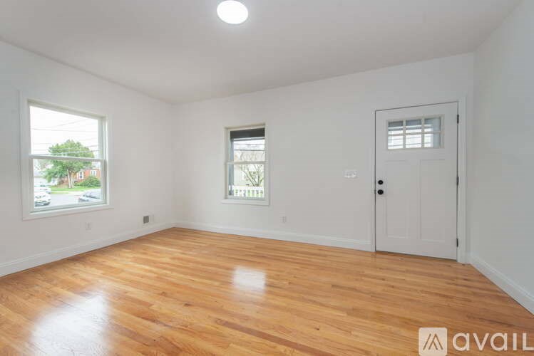 A room with wooden flooring and white walls, with a window and a door.