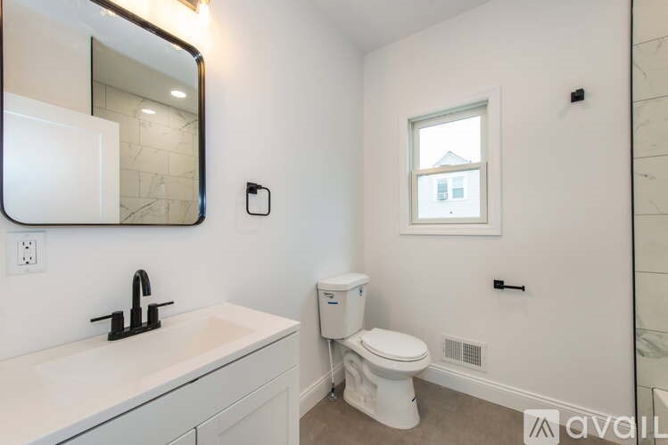 A white bathroom with a toilet, sink, mirror, and window.