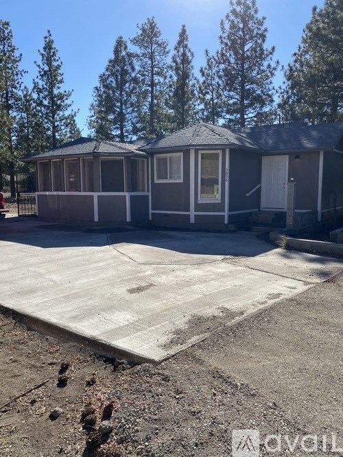 A house with a grey roof and a white door is surrounded by trees.