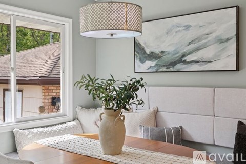 A living room with a large painting on the wall and a plant in a vase on the coffee table.
