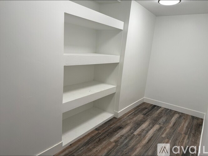 A room with white walls and wooden flooring with three shelves.