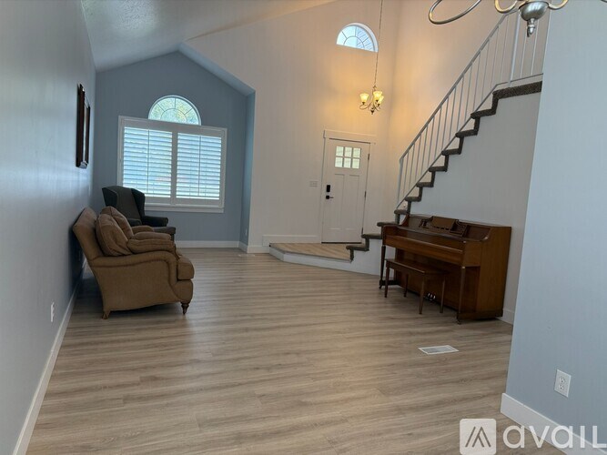 A living room with a brown couch, a piano, and a staircase.