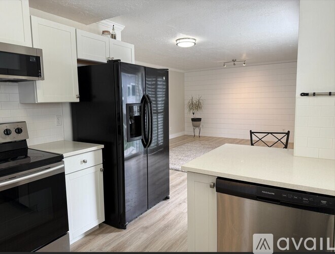 A black refrigerator is in a kitchen with white cabinets.