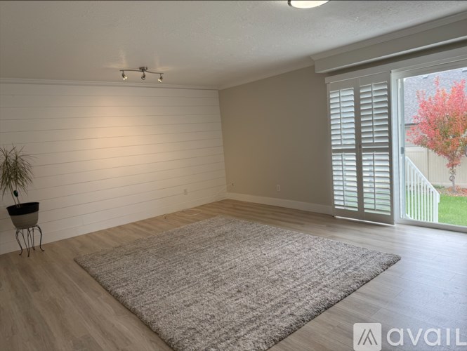 A room with a grey rug, wooden floor, and a sliding glass door.