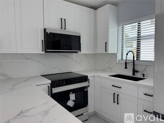 A kitchen with white cabinets and a black microwave.