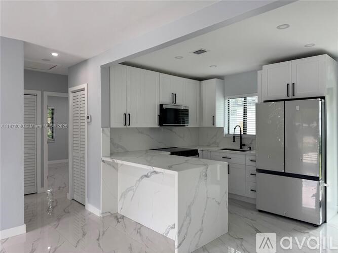 A modern kitchen with white cabinets and marble countertops.