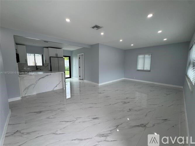 A spacious room with marble flooring and a kitchen area with a countertop and cabinets.