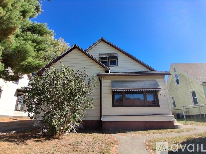 A house with a brown roof and a white wall is surrounded by a fence.