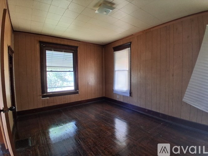 A room with wooden walls and floor and two windows.