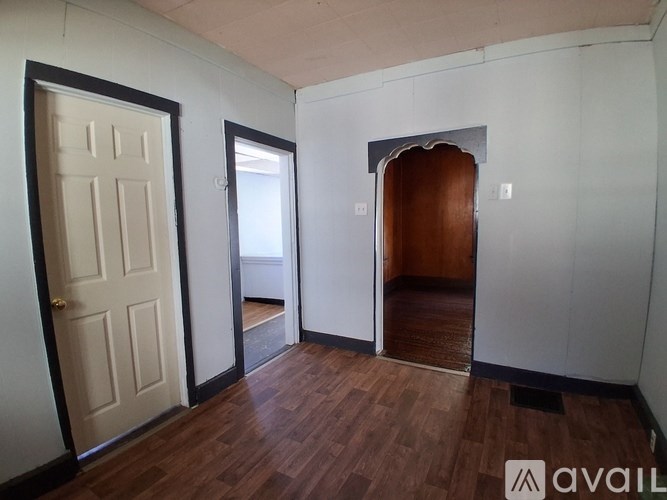 A room with a white door, a white wall, and a wooden floor.
