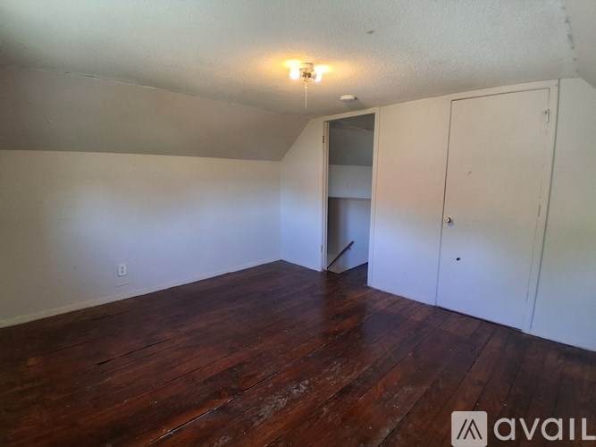 A room with wooden floors and white walls, with a doorway leading to another room.