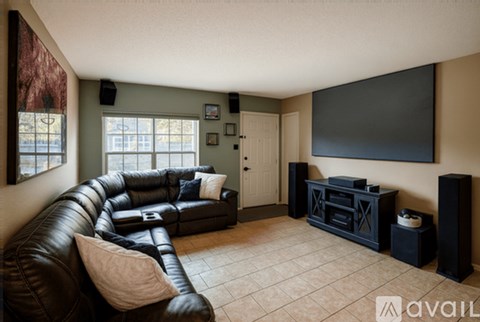 A living room with a black leather couch and a flat screen TV mounted on the wall.