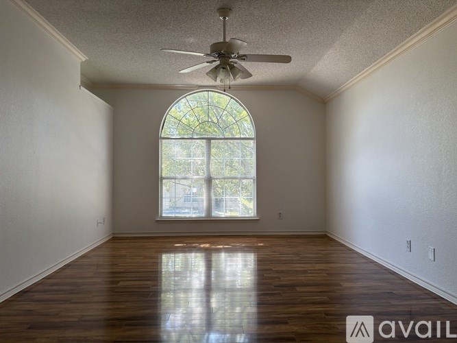 A room with a fan and a window with a view of trees.