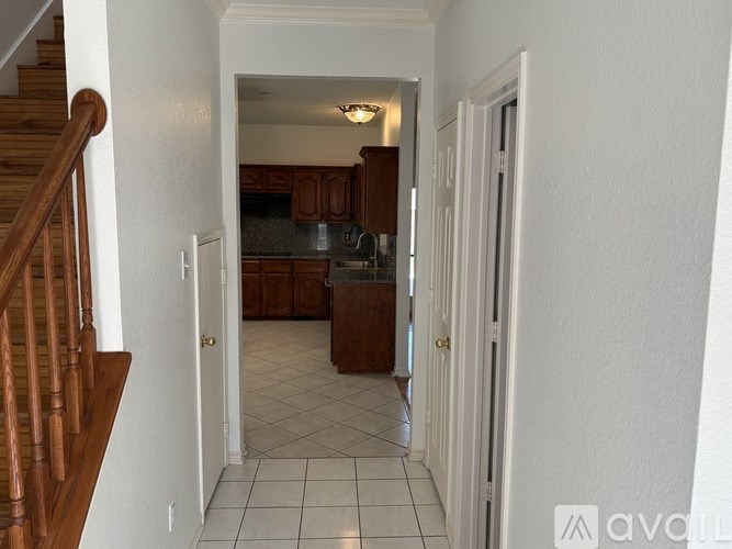 A hallway with a staircase on the left and a kitchen in the background.