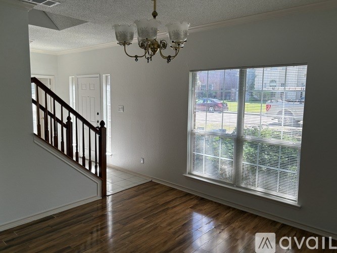 A room with a chandelier, a staircase, and a window overlooking a parking lot.