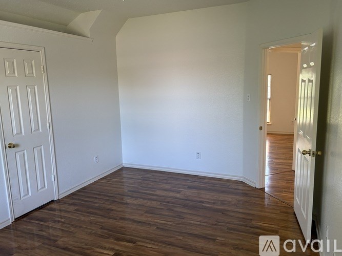 A room with wooden floors and white walls, with a door on the left and another door on the right.