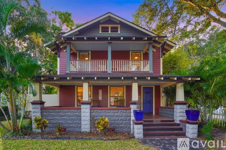 A house with a red front and a blue door is surrounded by greenery.