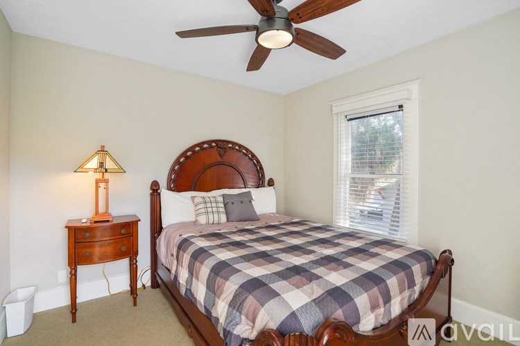 A bedroom with a bed, a ceiling fan, and a lamp on a nightstand.
