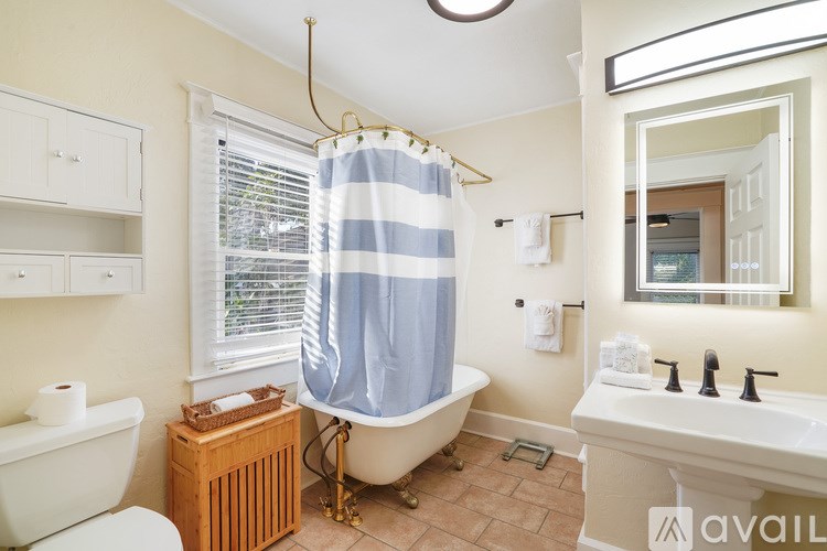 A bathroom with a white tub, a blue striped shower curtain, and a wooden radiator.