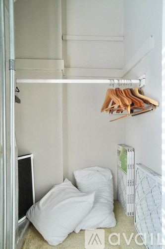A white closet with clothes hanging and a bed with a white pillow.