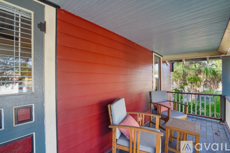 A red wooden house with a white door and a balcony with chairs.