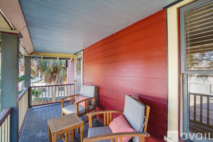 A balcony with a red wall and a wooden table and chairs.