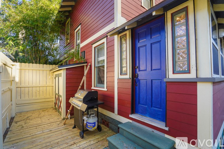 A red house with a blue door and a grill on a wooden deck.