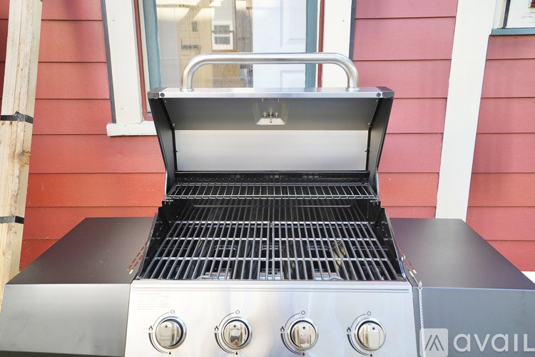 A grill with four burners is on a red wall.