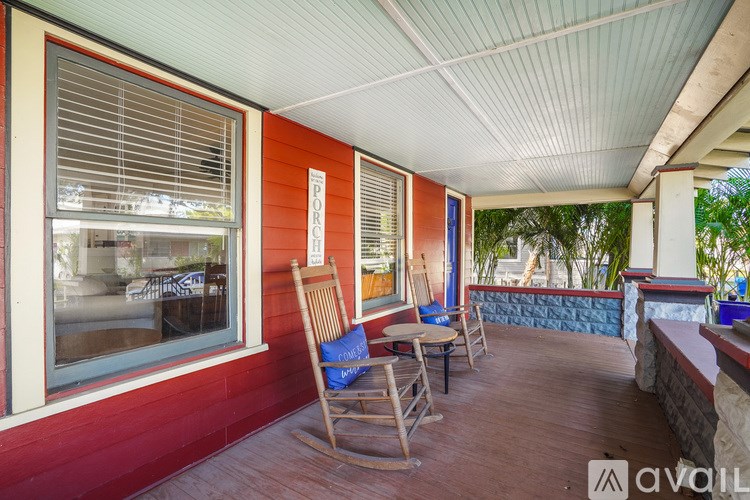A porch with a red wall and a wooden rocking chair.
