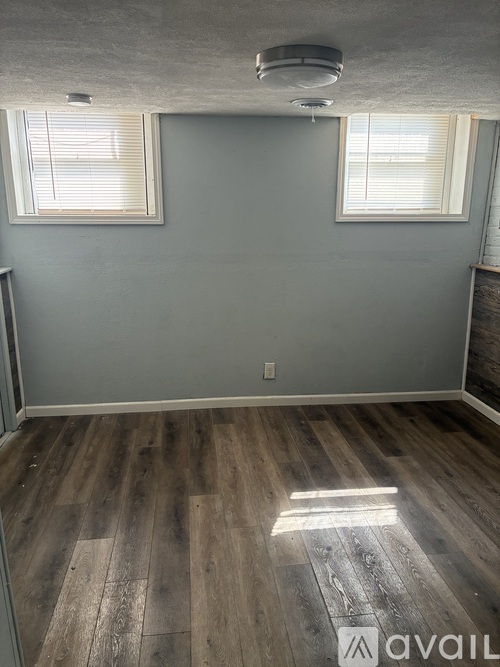 A room with wooden flooring and two windows.