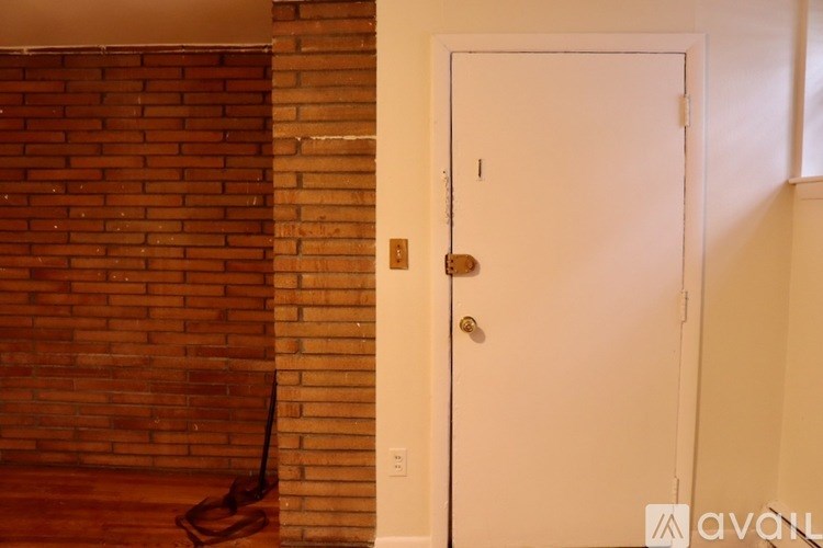 A white door with a gold handle is in a room with a brick wall.