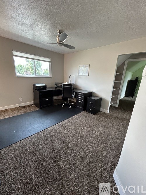A room with a desk, chairs, and a ceiling fan.