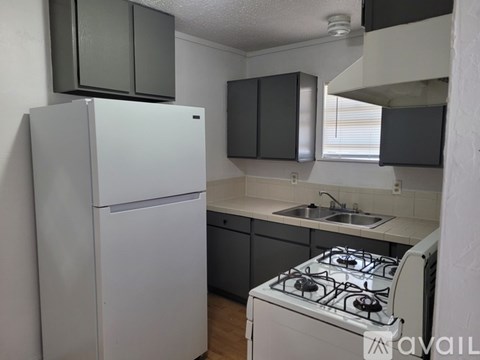 A white refrigerator stands in a kitchen with a stove and sink.