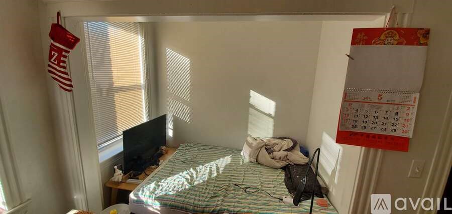A bedroom with a bed, a TV, a window with blinds, and a calendar hanging on the wall.