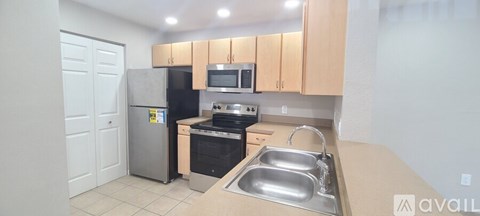 A kitchen with a refrigerator, microwave, oven, sink and cabinets.