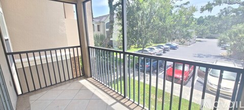 A balcony with a black railing and a view of a parking lot and trees.