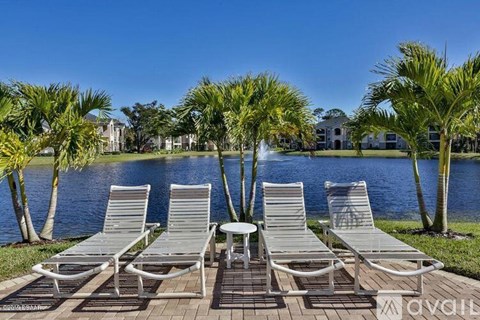 A row of lounge chairs are set up on a patio overlooking a body of water.