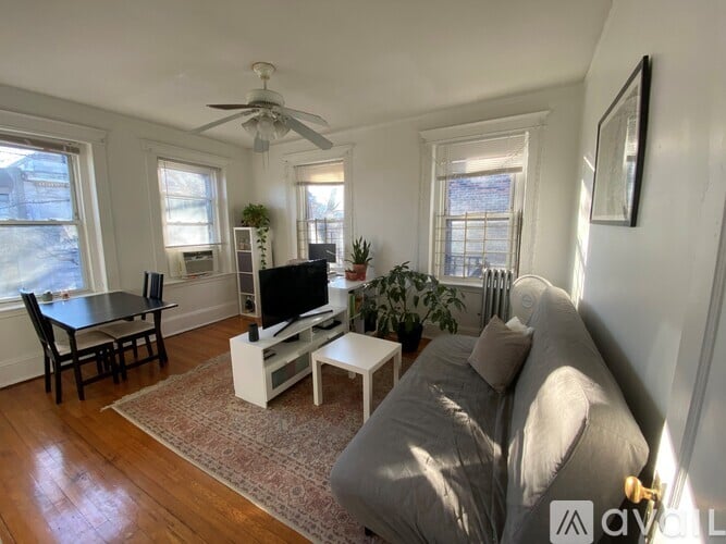 A living room with a grey couch, a black table, a television, and a ceiling fan.